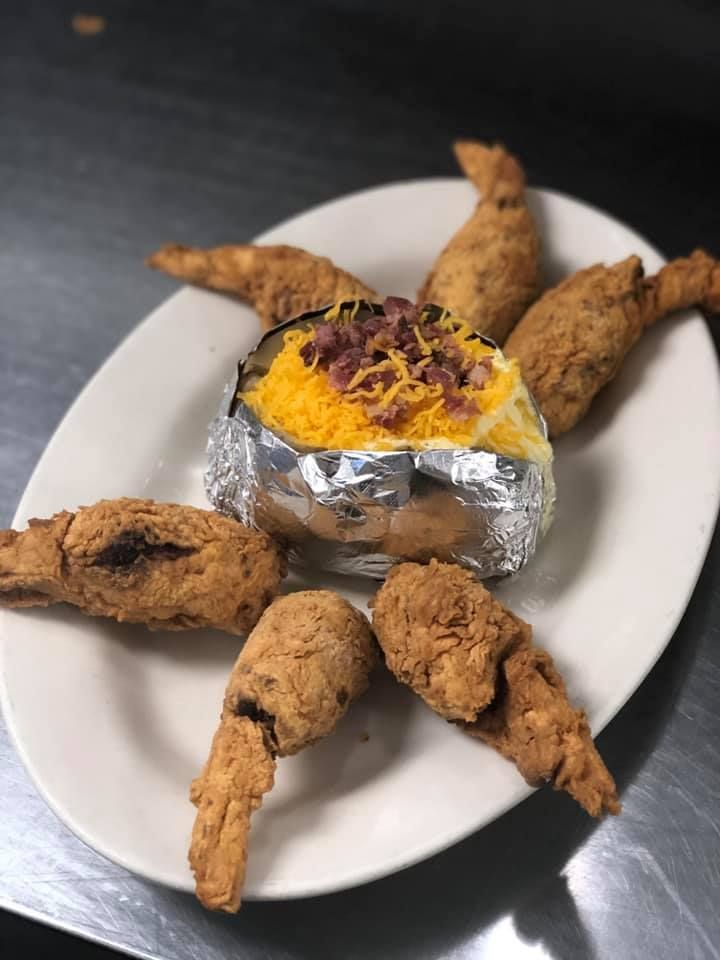 Foil-wrapped baked potato topped with cheese and bacon, surrounded by fried potato wedges on a white plate