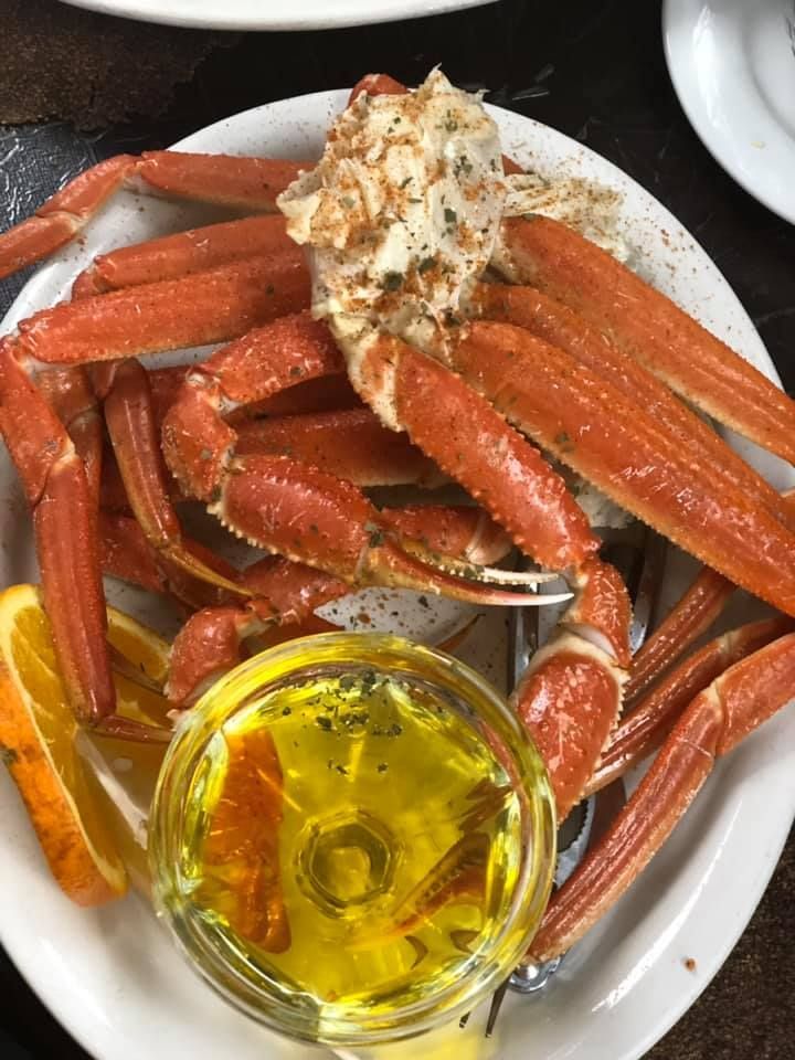 Plate of cooked crab legs with melted butter and seasoning on a white dish