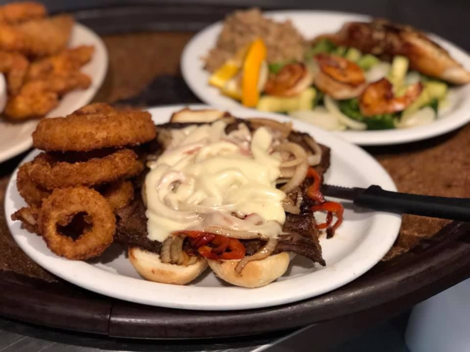 Plates of fried appetizers and a cheesesteak sandwich on a wooden table