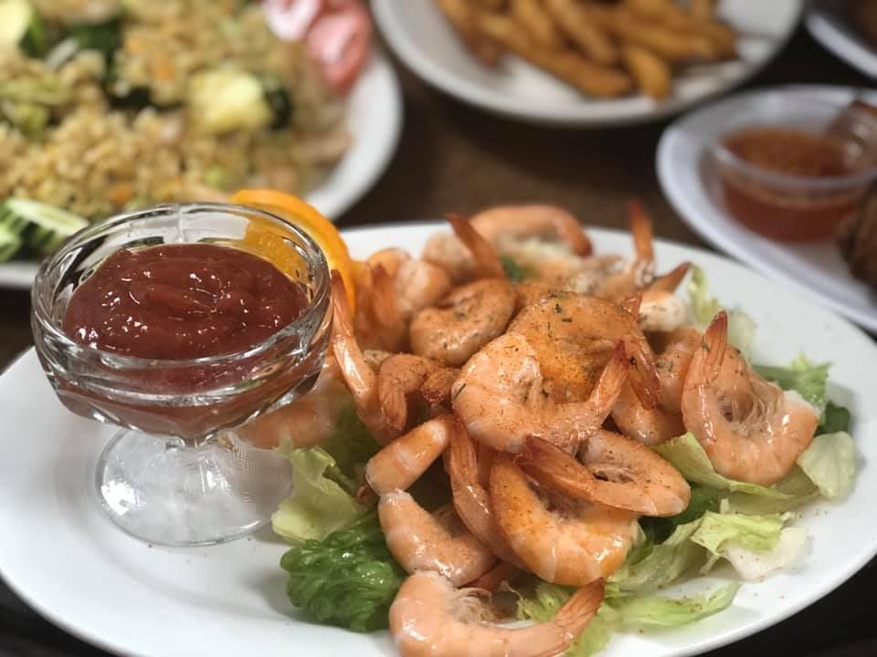 Grilled shrimp on lettuce with dipping sauce in a glass bowl, served on a white plate.