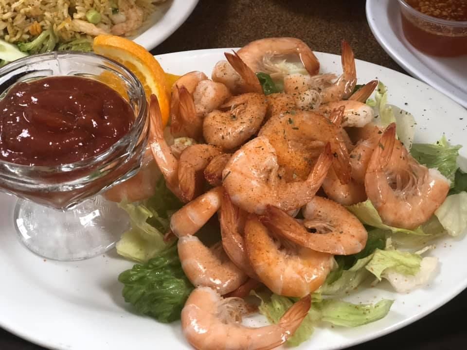 Shrimp cocktail on a white plate with lettuce garnish and a side of cocktail sauce