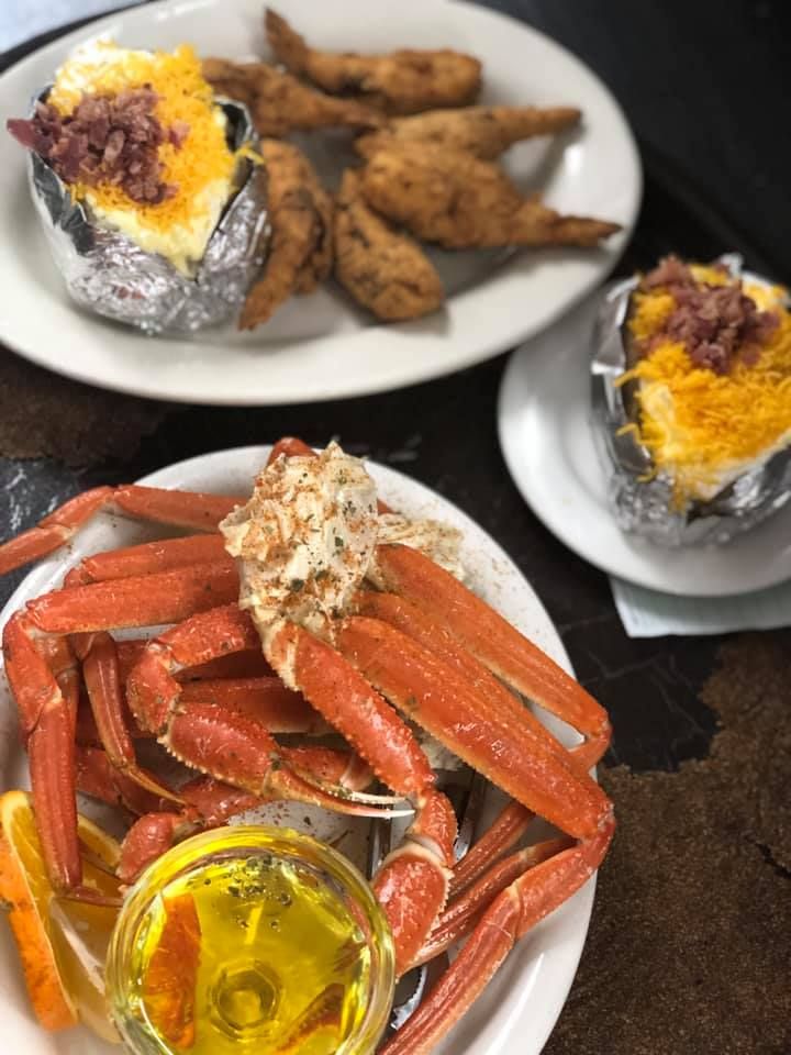 Crab legs with melted butter and two baked potatoes topped with cheese and bacon on white plates