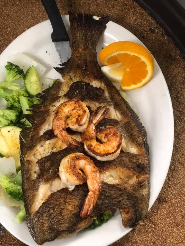 Plated grilled whole fish topped with shrimp, served with cucumber, potato, and orange slices