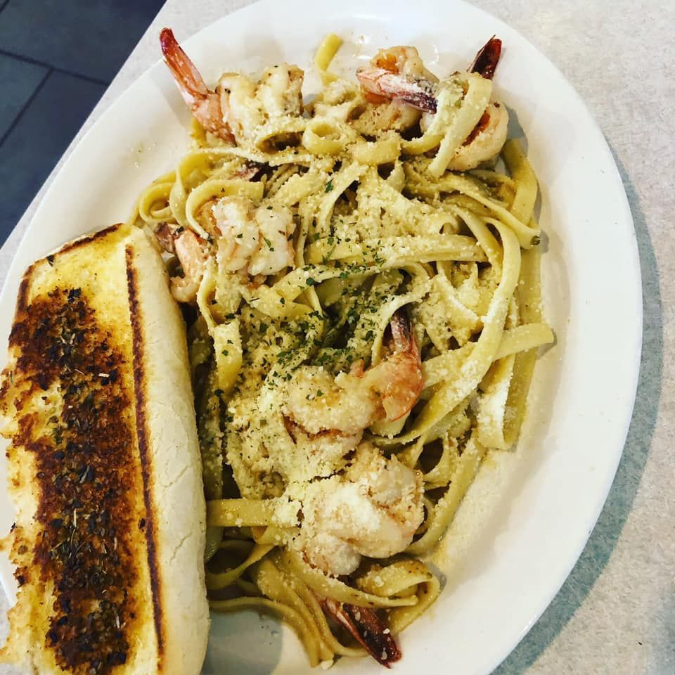 Pasta with shrimp in creamy sauce on a white plate, with a slice of garlic bread beside it.