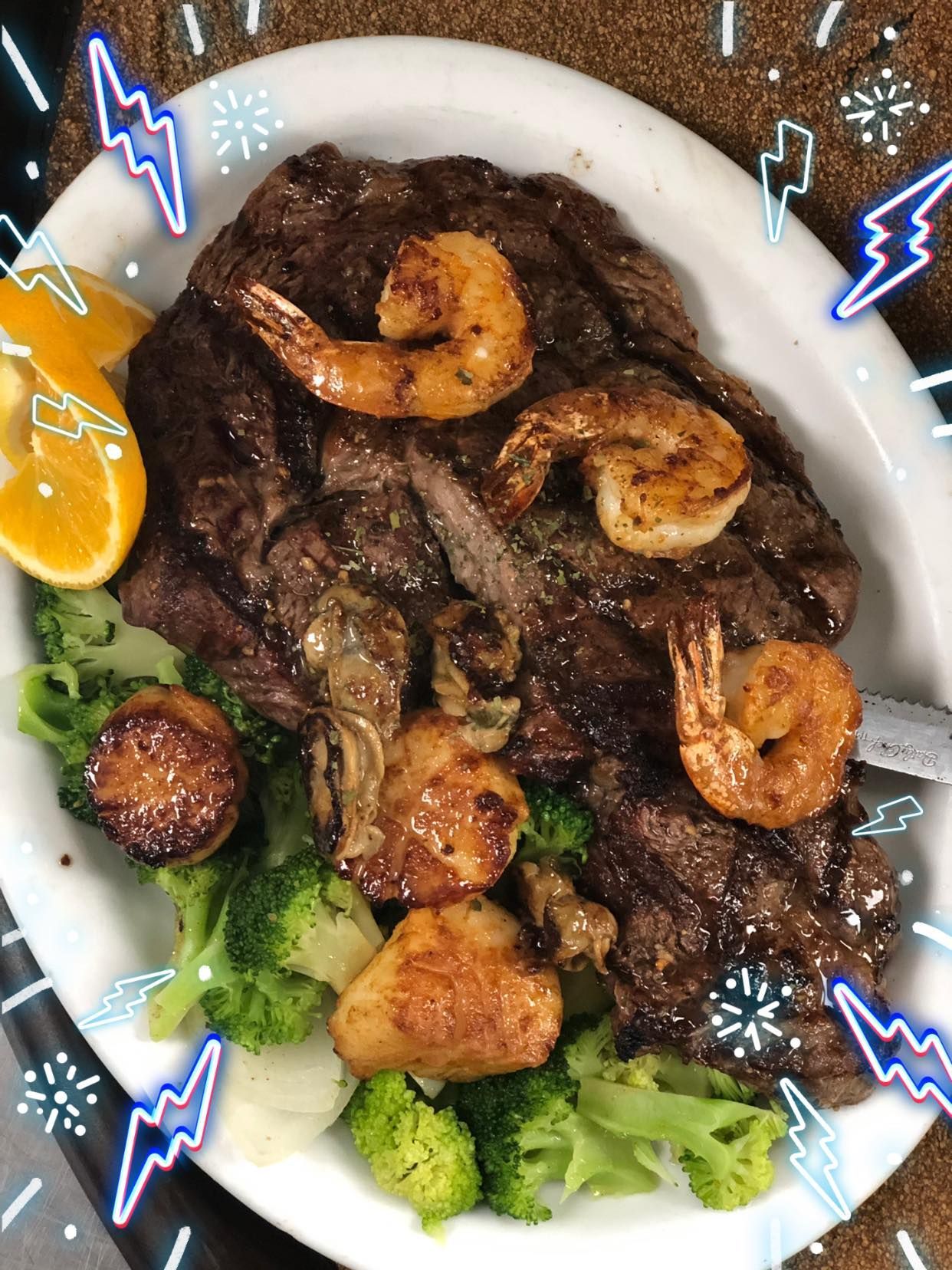 Grilled steak and shrimp over broccoli on a white plate with orange slices and garnish