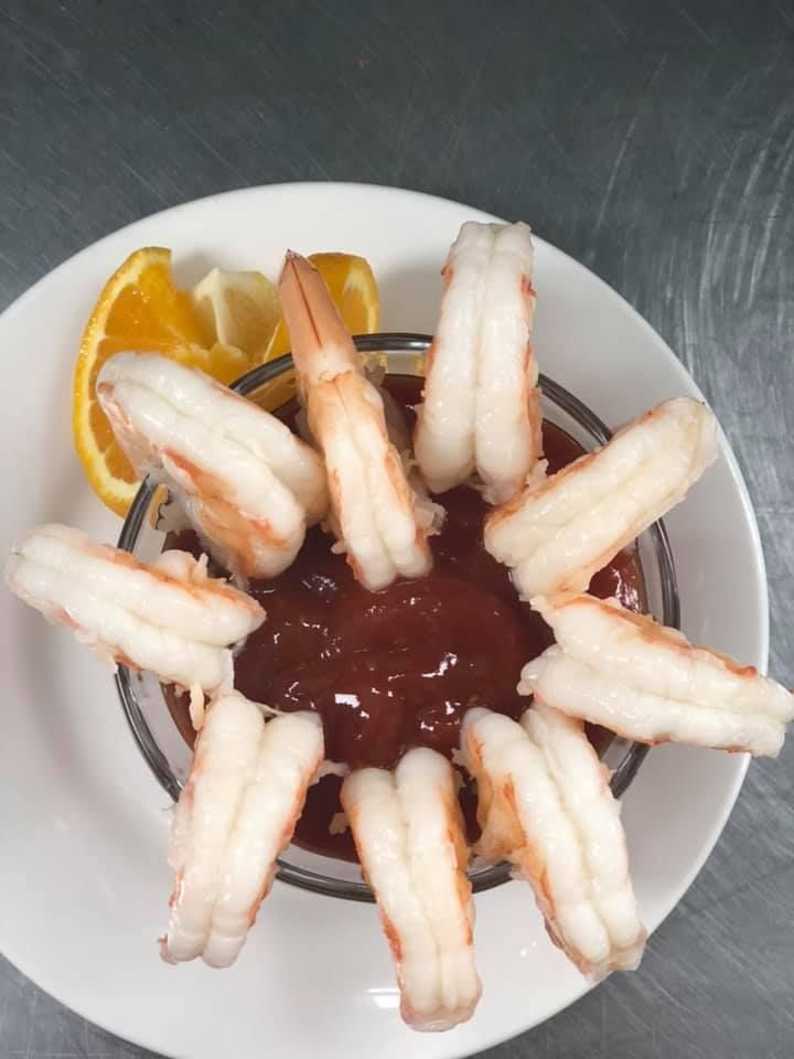 White plate with shrimp arranged around a bowl of dark sauce and an orange slice on a metal table