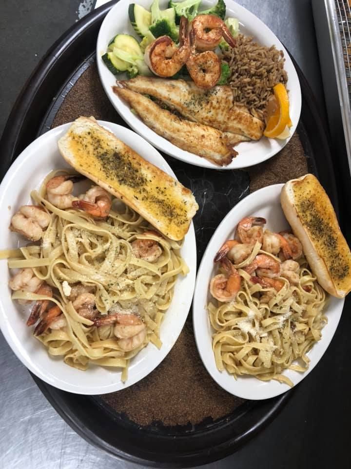 Plates of assorted seafood pasta and grilled fish arranged on a black tray.