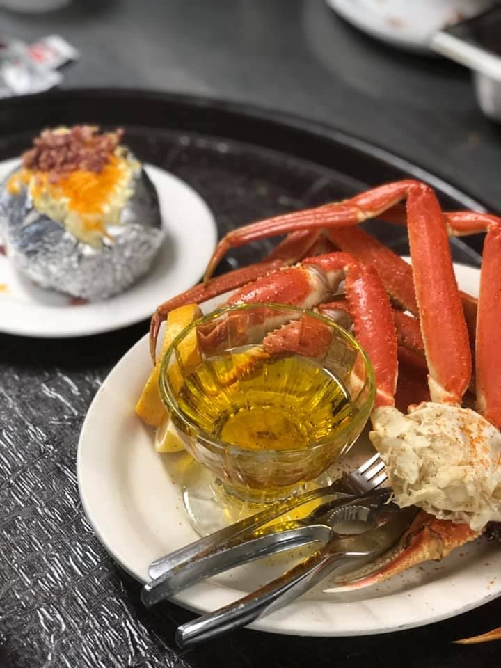 Plate of crab legs with melted butter and a side of baked potato on a table