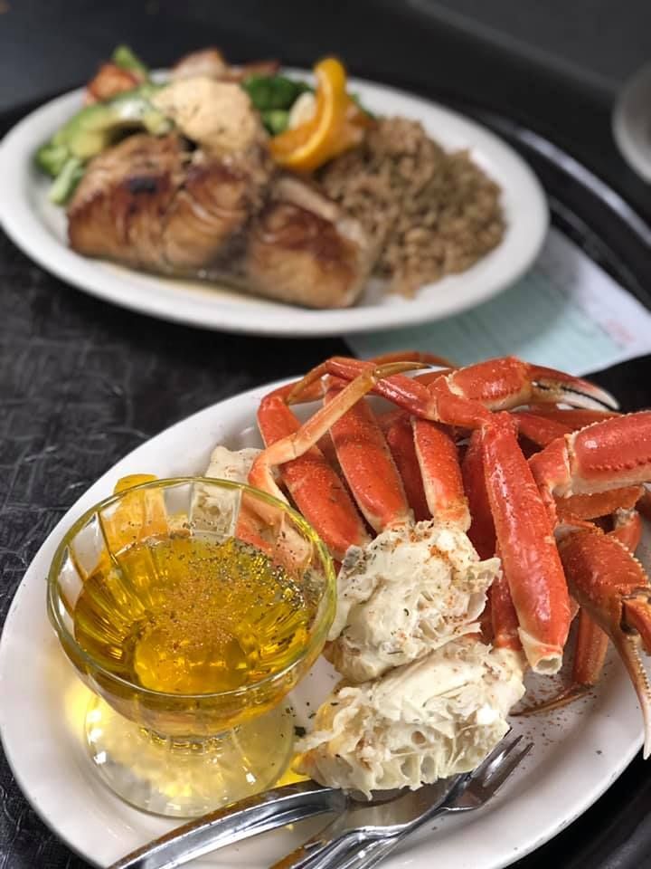 Crab legs with melted butter on a white plate, with a lobster dinner blurred in the background.