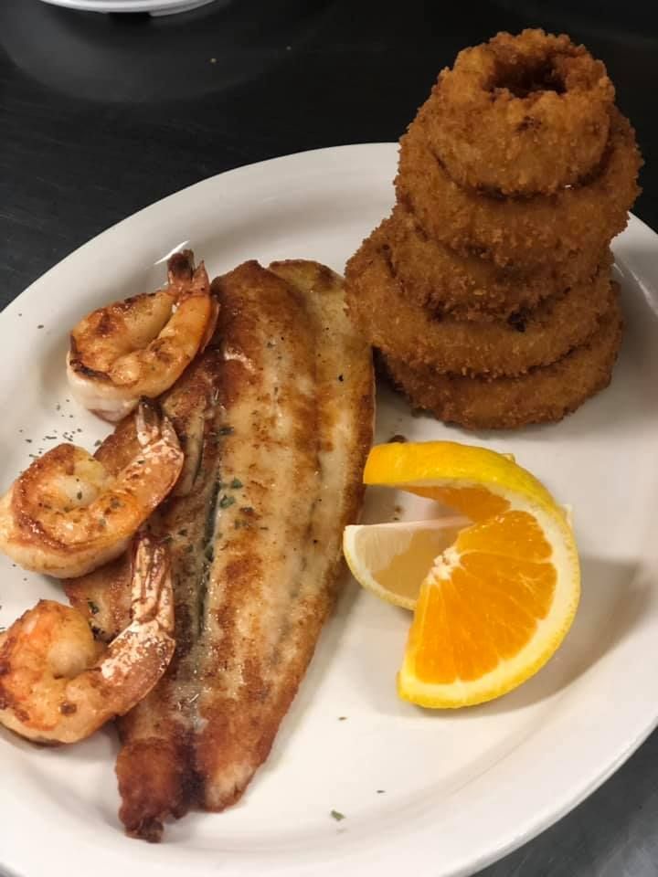 Grilled fish and shrimp with orange slices and onion rings on a white plate