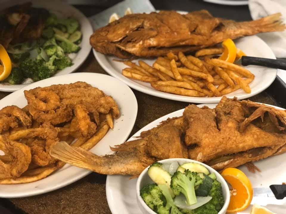Plates of fried fish and fries with broccoli and lemon slices on a table