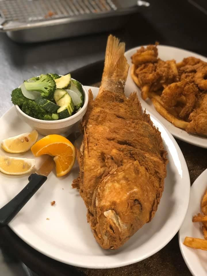 Plate with fried whole fish, lemon wedges, cucumber salad, and fried chicken on a restaurant table