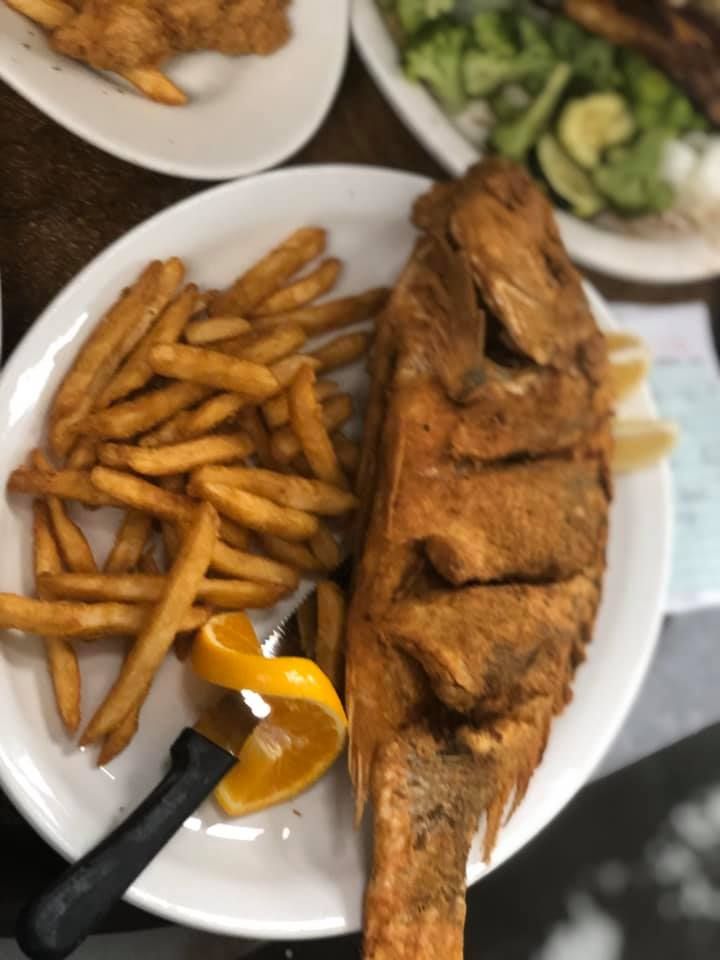 Plate of fried fish with French fries and salad, with a lemon wedge and sauce on the side.