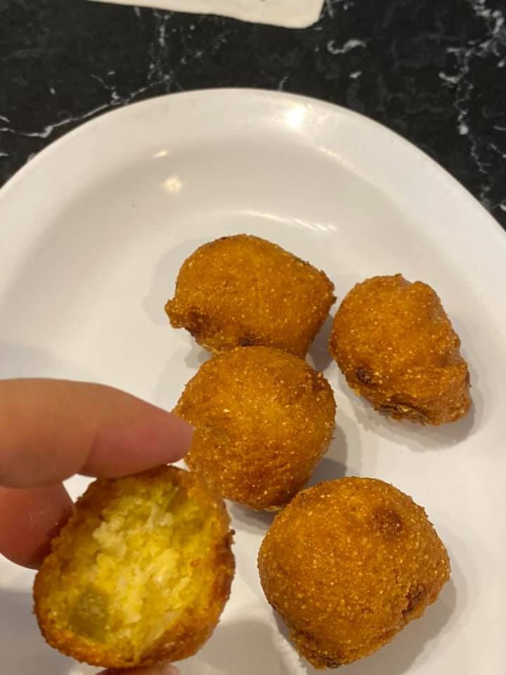 Hand holding a bitten golden-brown fried snack on a white plate with four more pieces
