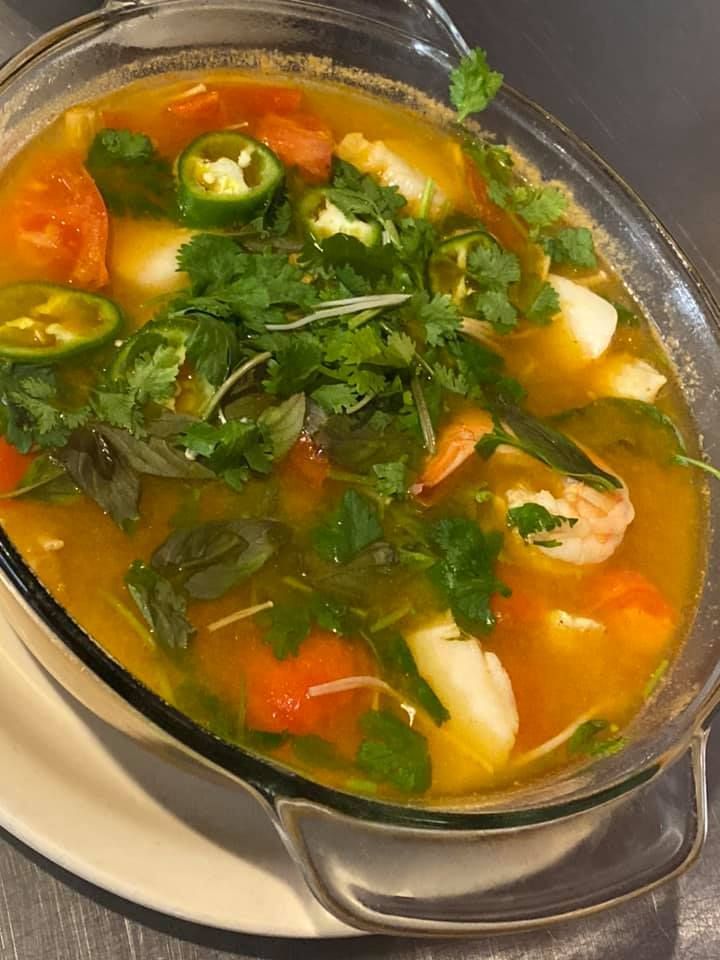 Bowl of colorful soup topped with herbs, jalapeños, and shrimp on a plate