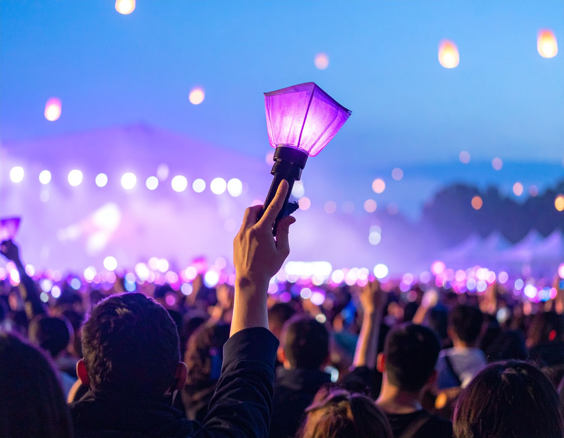 Crowd at an outdoor concert waving purple glow sticks at dusk