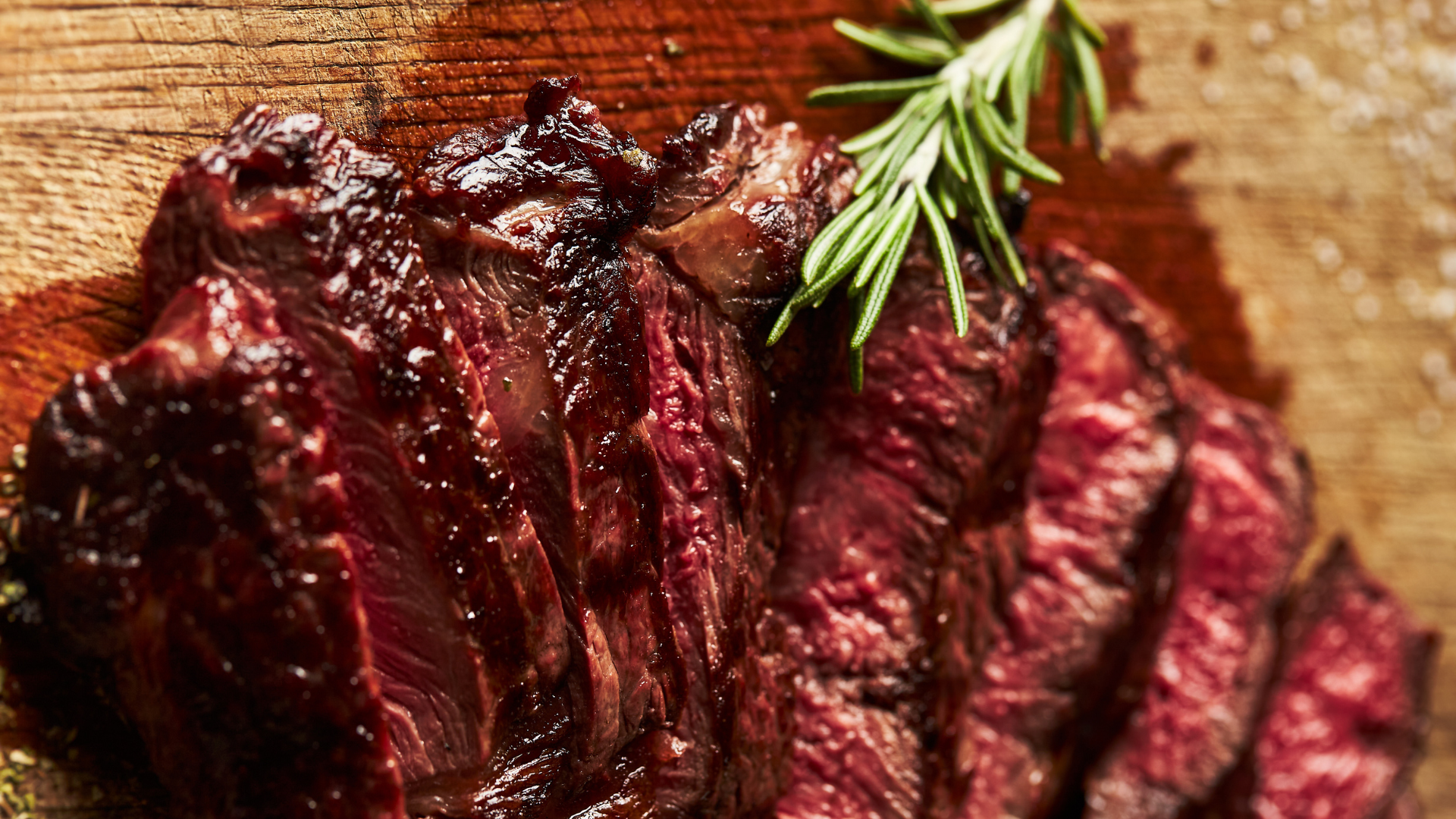A close up of a steak on a wooden cutting board with rosemary.