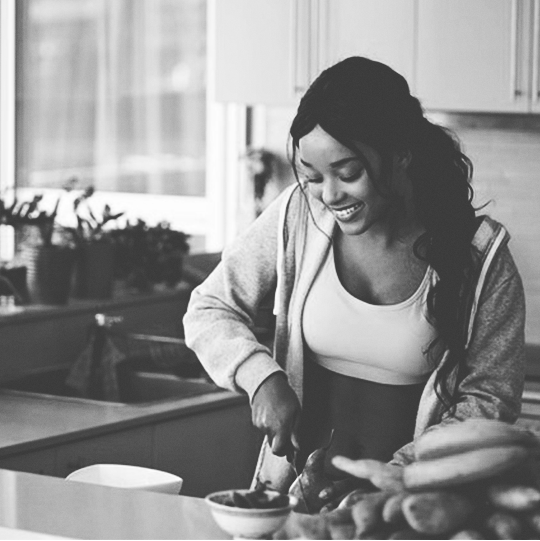 Person smiling while preparing food in a kitchen, with fruit on the counter