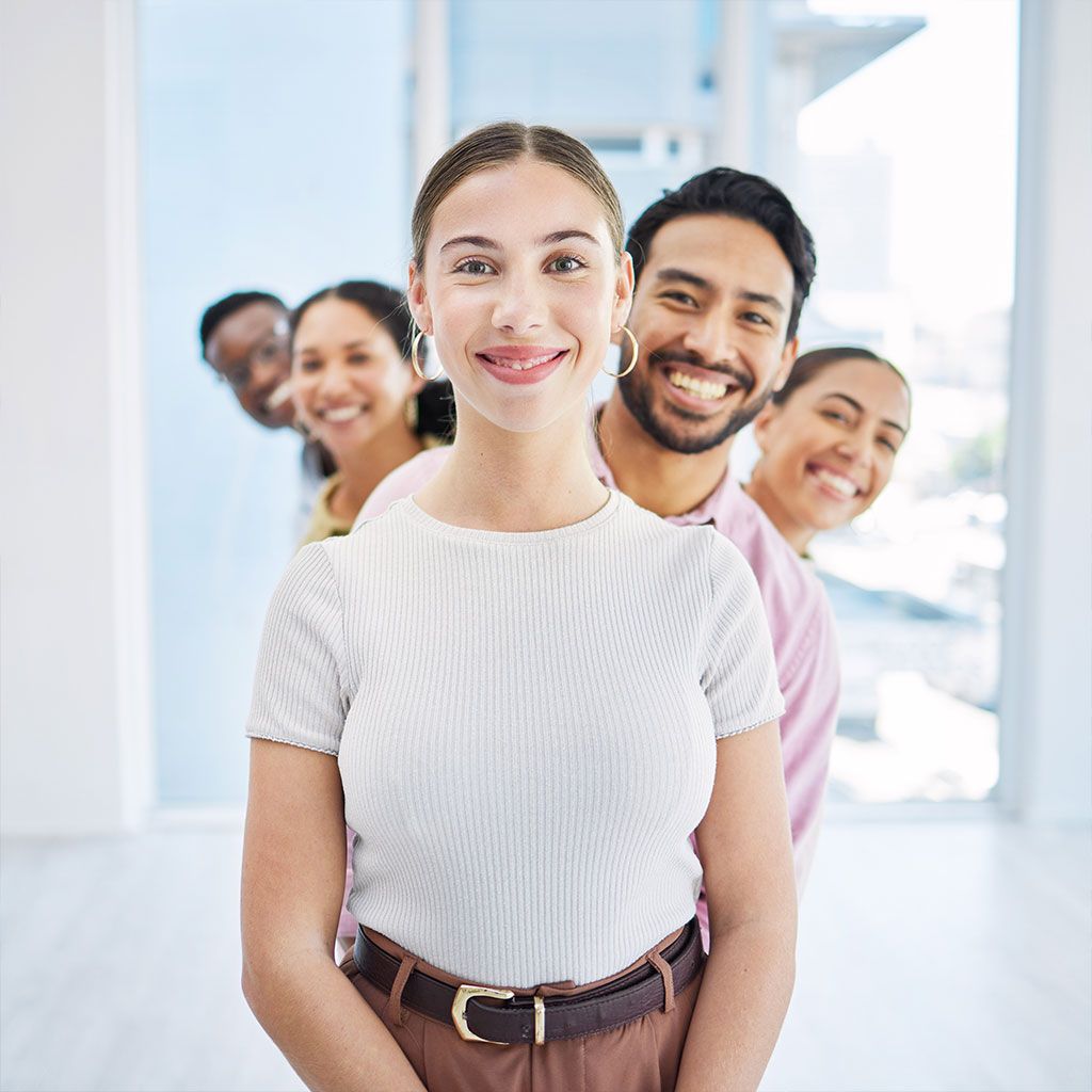 Four smiling people standing in a bright office hallway, with a woman in front and three behind her.