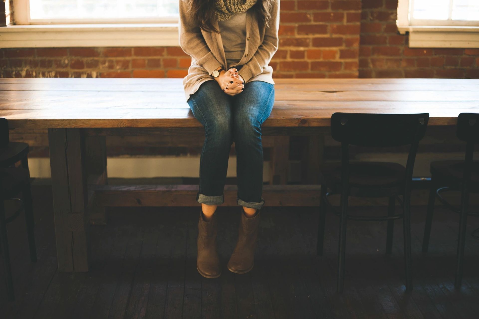 Person sitting on a wooden bench by a bright window, wearing jeans and brown boots