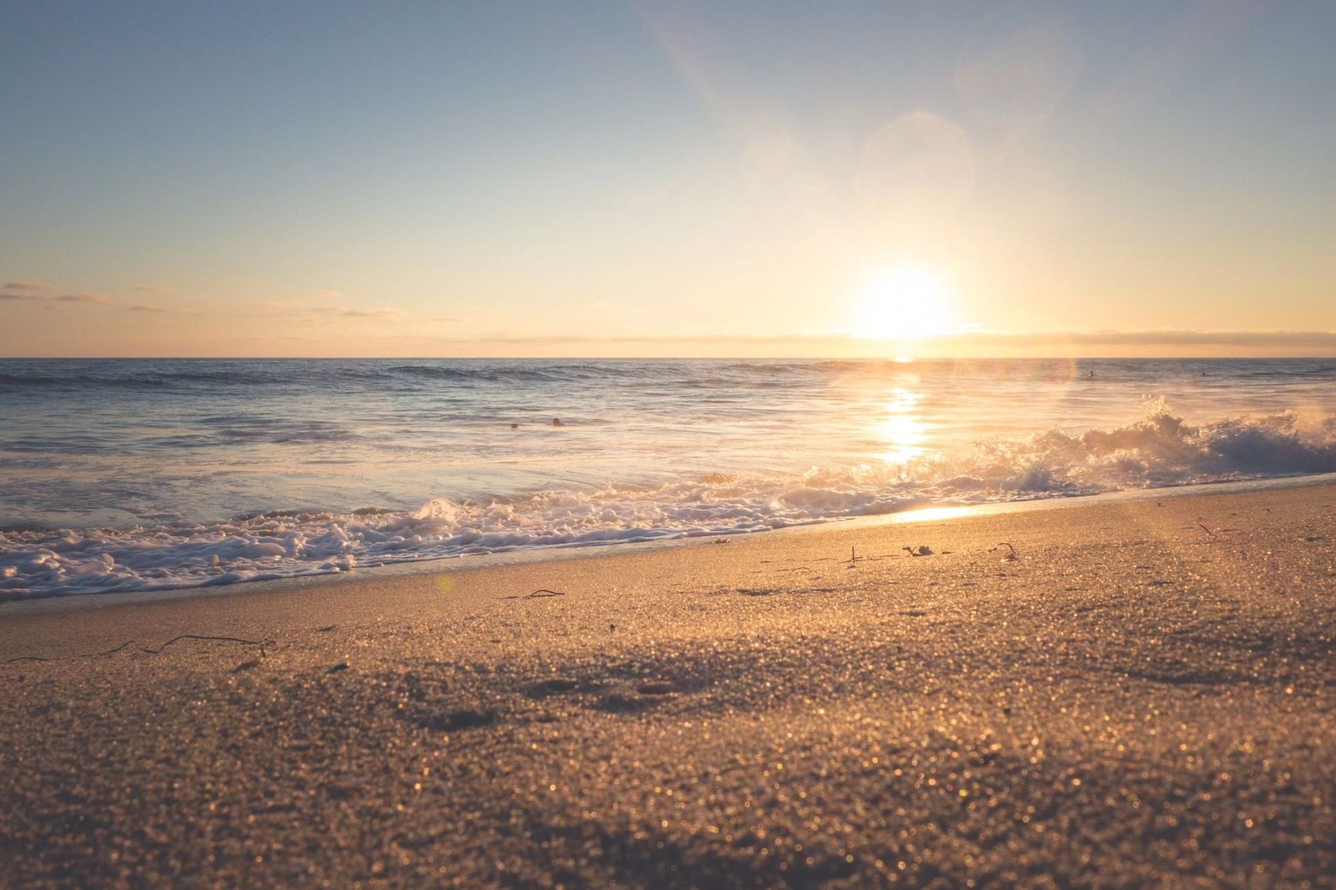 Sunrise over a sandy beach with gentle waves and golden reflections on the water
