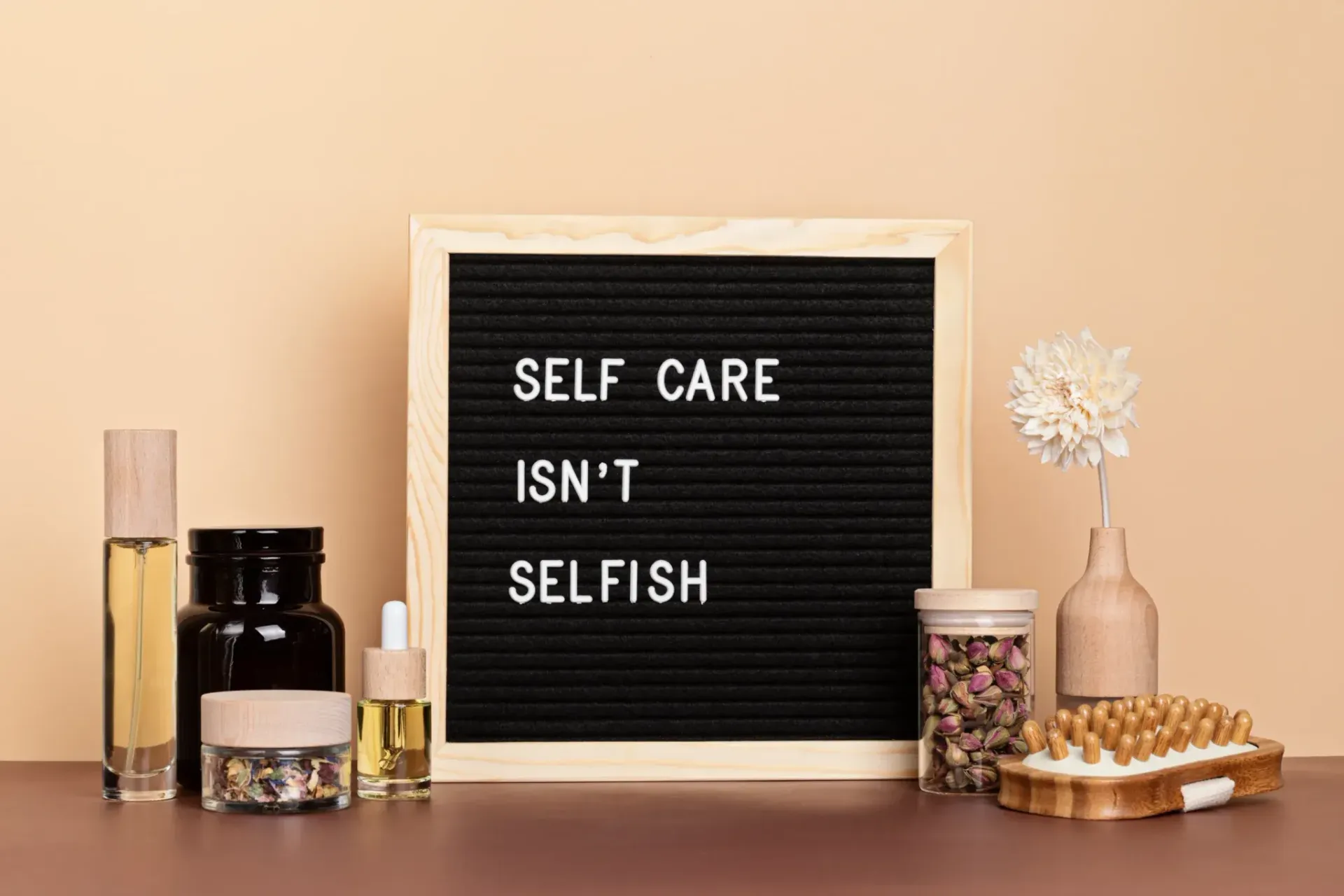 Letter board reading “SELF CARE ISN’T SELFISH” with candles, jars, and a flower on a table