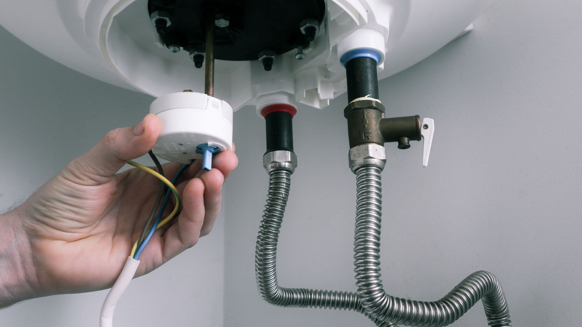 Hand adjusting a bathroom sink light fixture with exposed wires and plumbing underneath