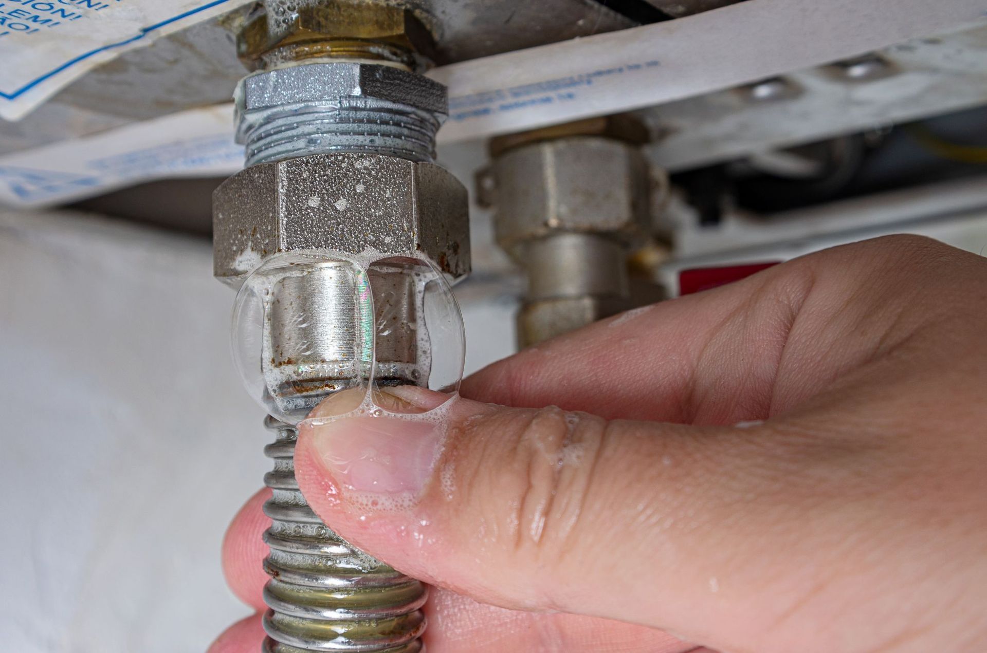Hand tightening a braided metal hose onto a plumbing valve under a sink
