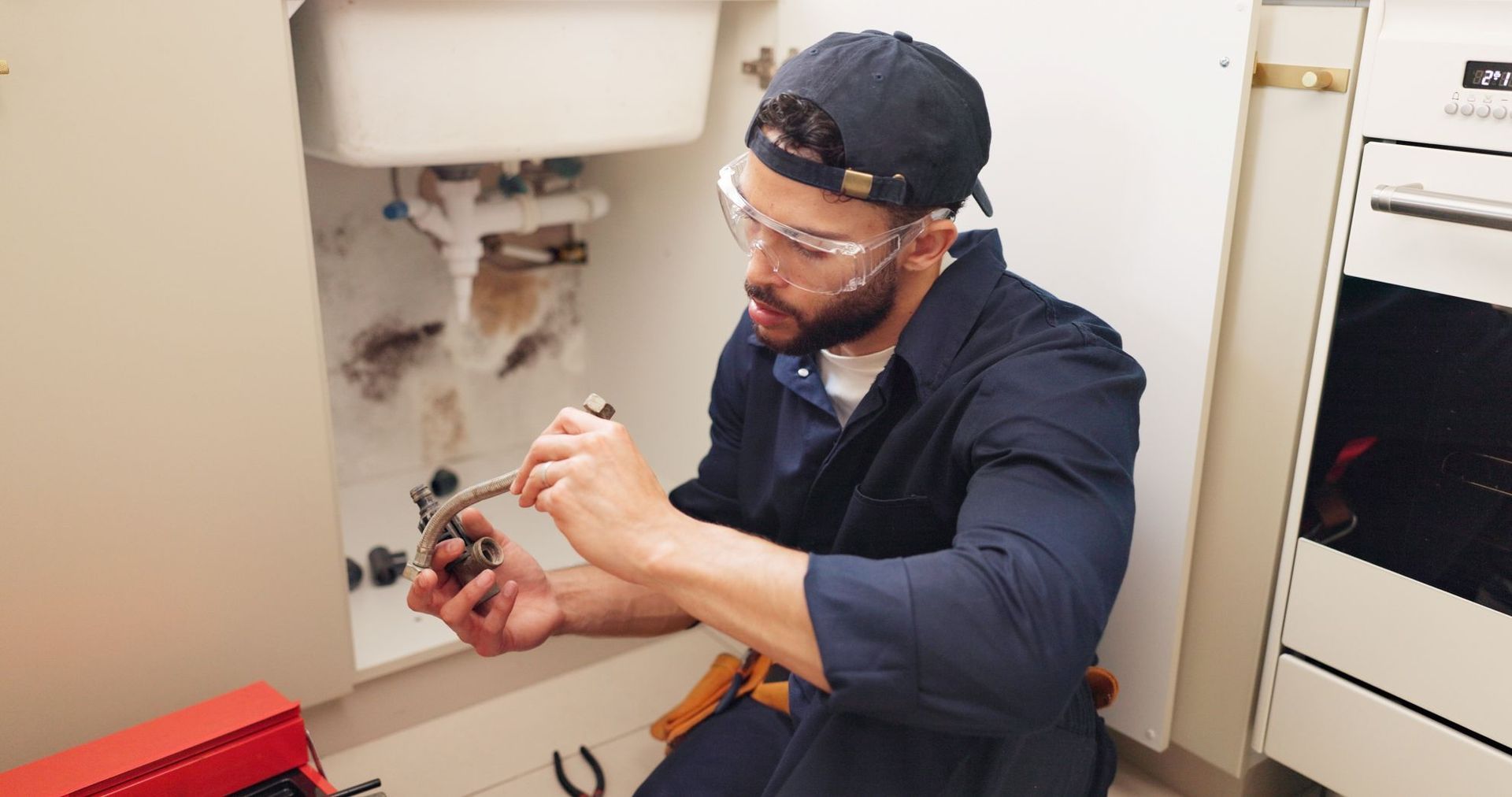 Technician inspecting a wall cavity with a tool, wearing gloves and safety glasses in a utility room.