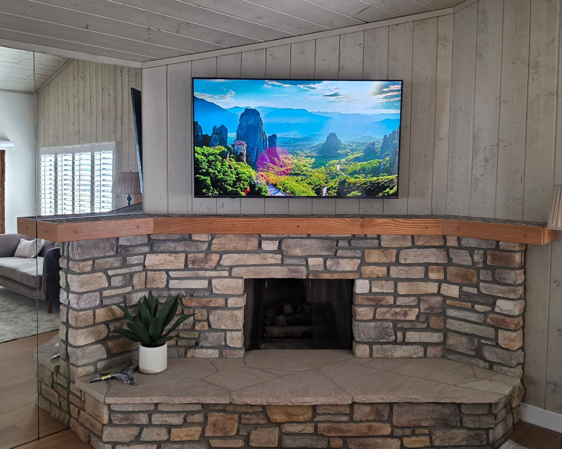 Stone fireplace in a cozy living room with a TV mounted above, showing a bright mountain landscape.