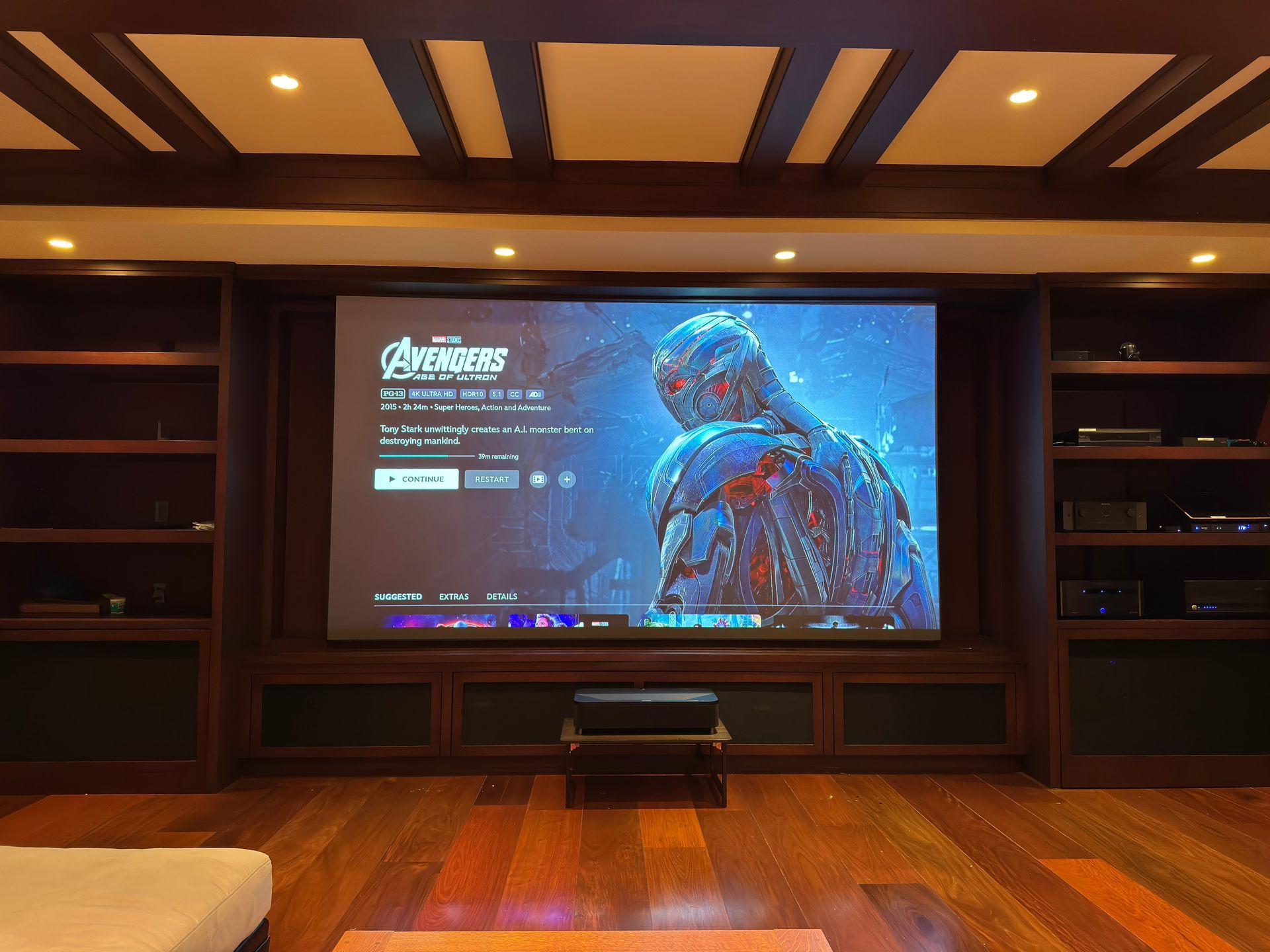 Home theater with a large TV displaying a game menu on a wood-paneled wall, warm recessed lighting.