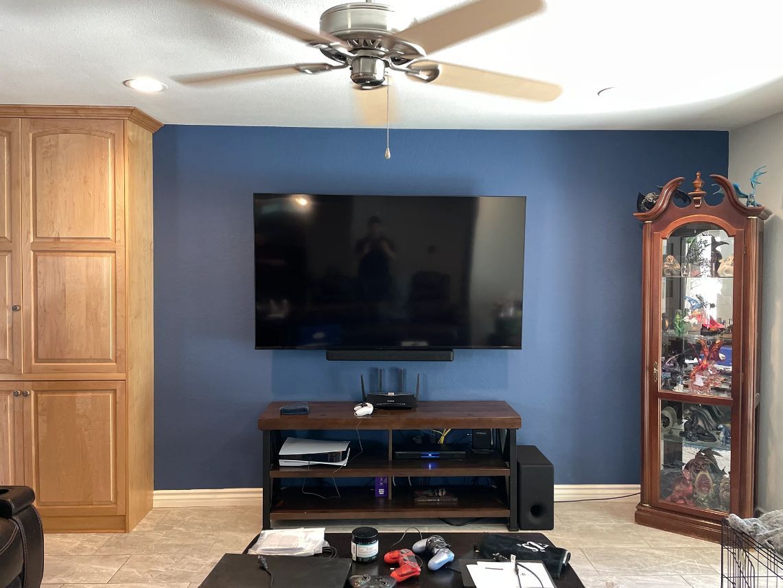 Living room with wall-mounted TV, blue accent wall, wood cabinet, and glass display cabinet.