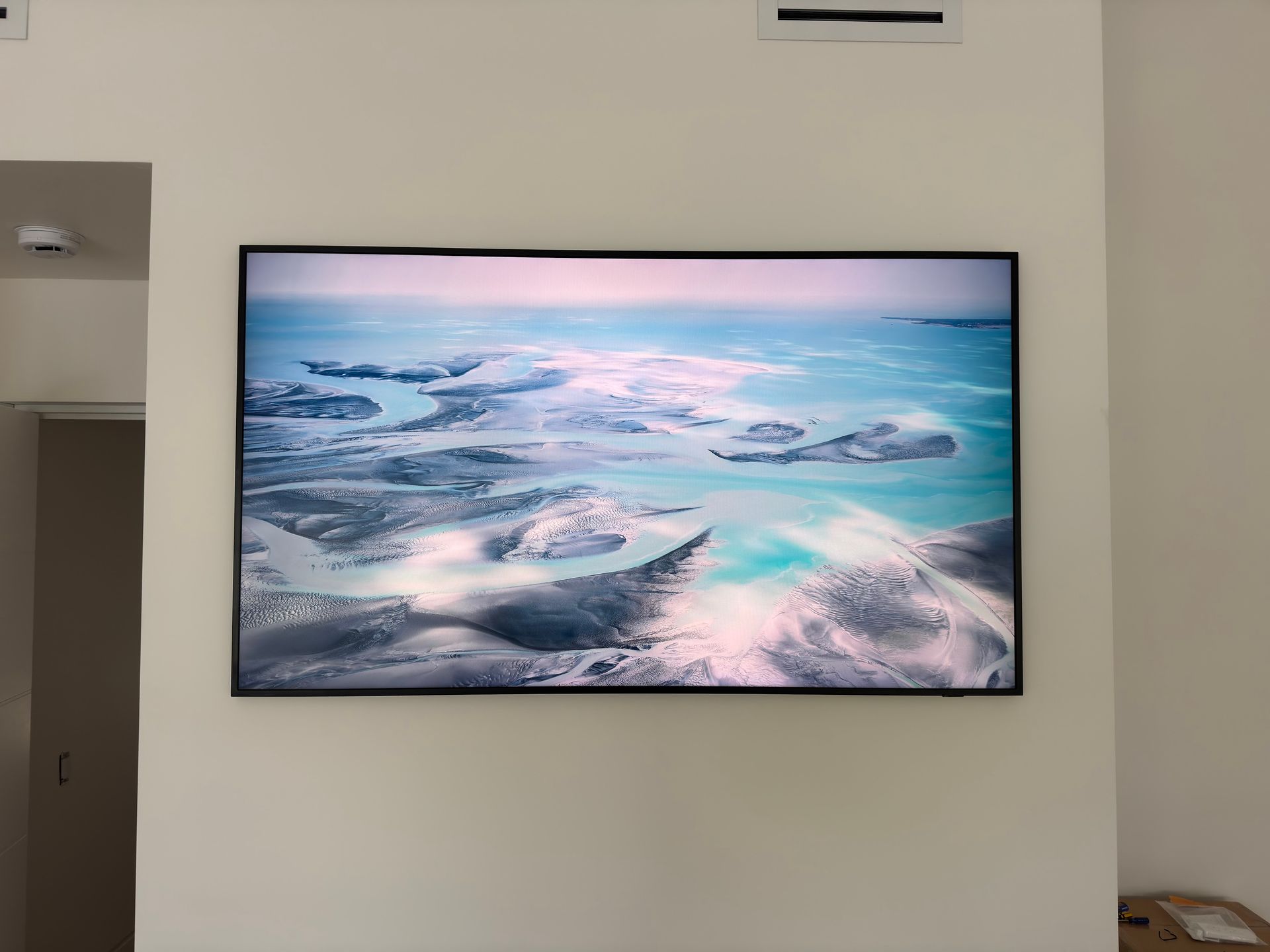 Wall-mounted TV displaying a pastel aerial seascape of snowy islands in a minimal room