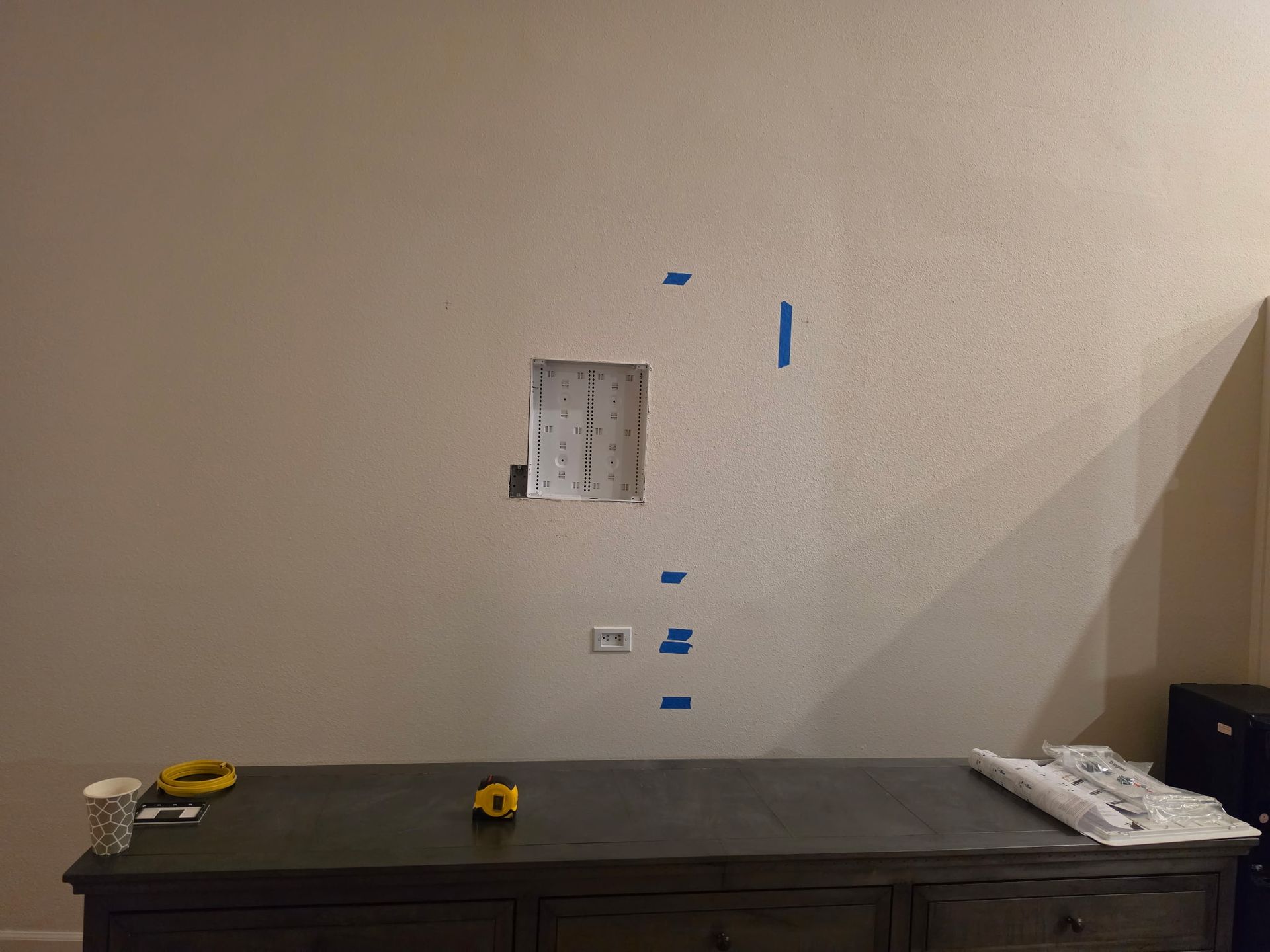Bare wall with marked outlet cutout above a workbench in a room under renovation