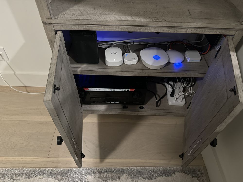 Open cabinet with networking equipment, power strips, and white devices on shelves.