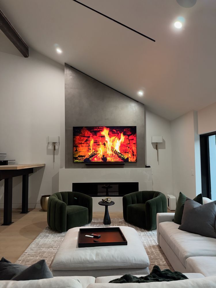 Modern living room with fireplace TV, vaulted ceiling, green chairs, white sofa, and large rug