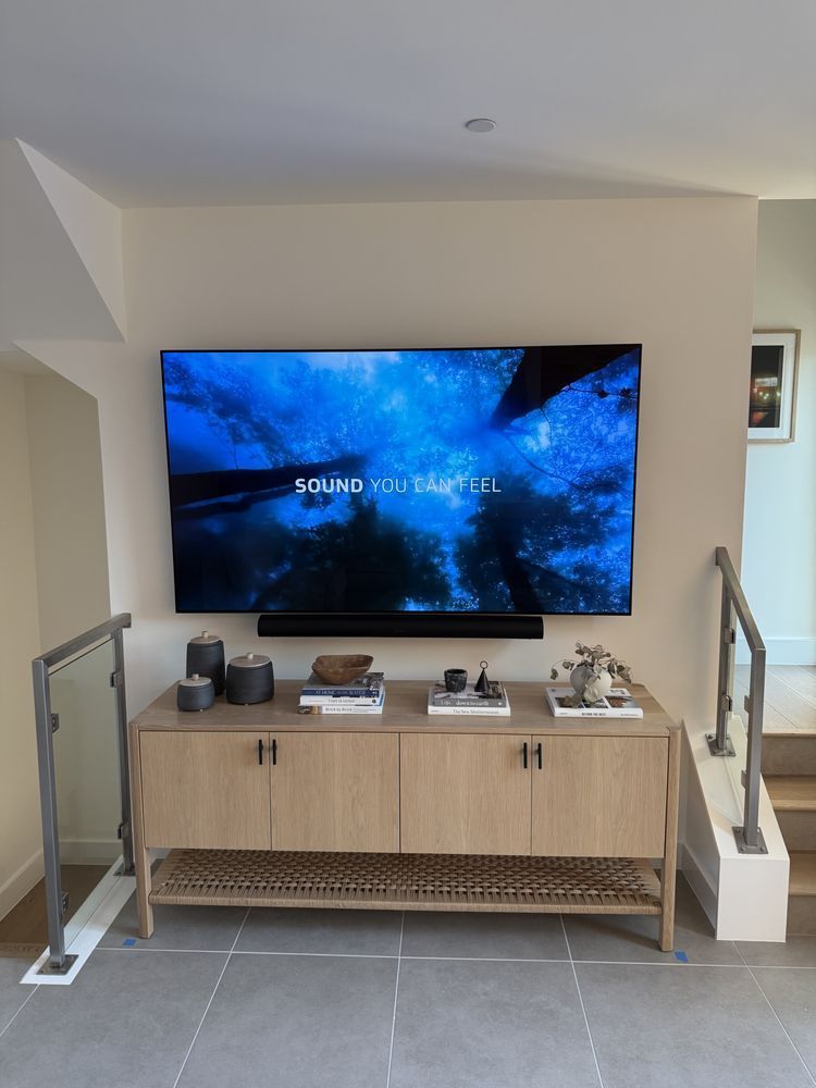 Wall-mounted TV above a light wood console in a modern living room with gray tile floor and stairs.