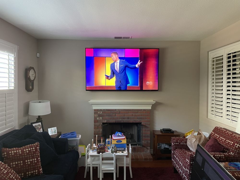 Living room with TV above fireplace showing a colorful dancer, flanked by windows and couches