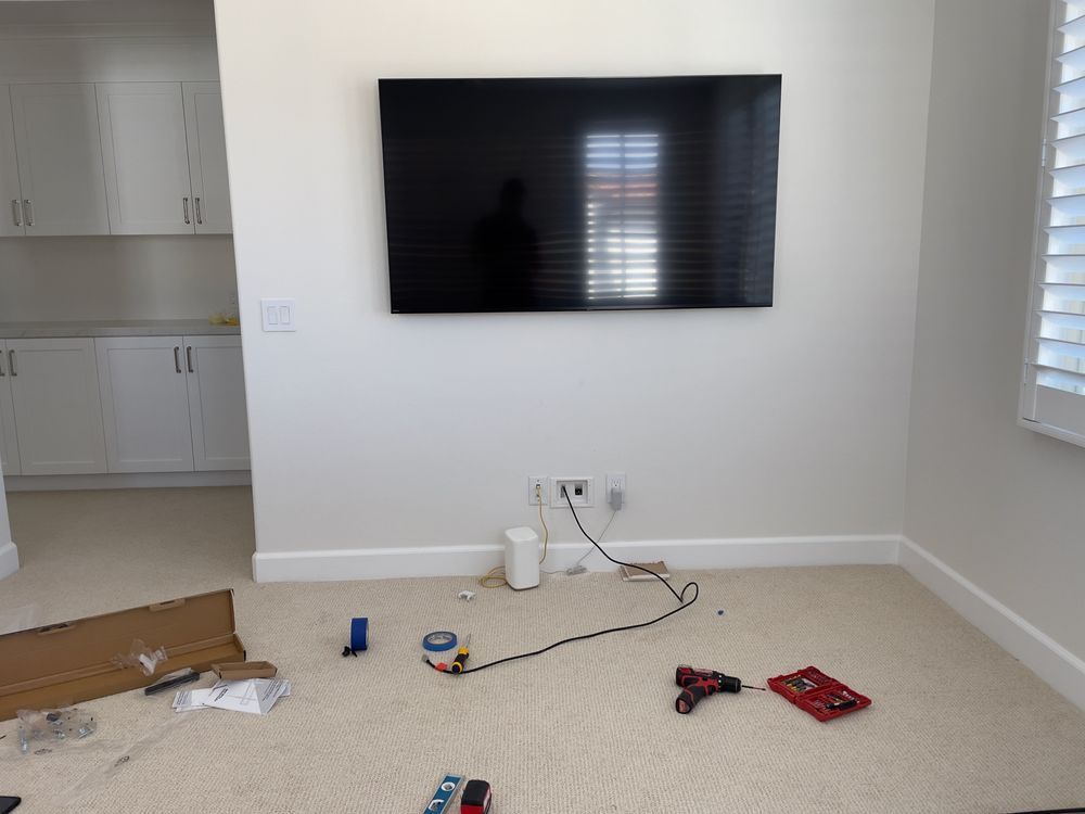 Living room with a wall-mounted TV, white cabinets, and tools and packaging on the floor.