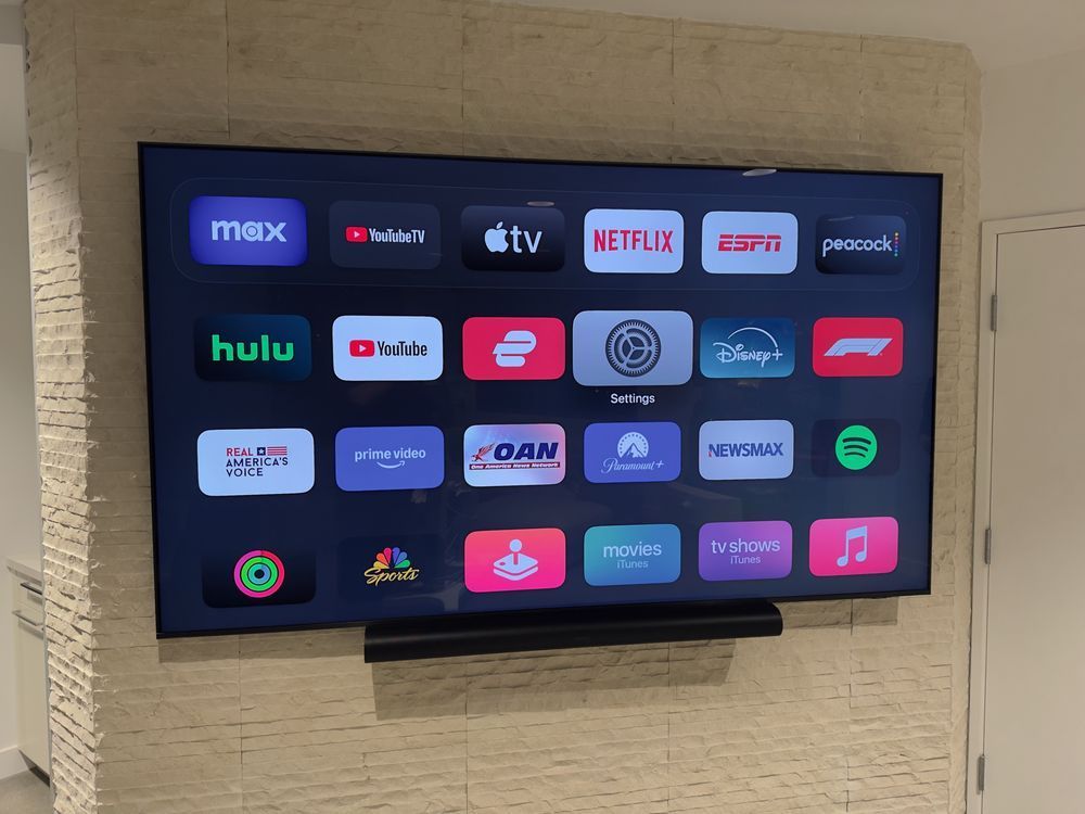 Wall-mounted TV showing a grid of streaming app icons on a dark screen in a room