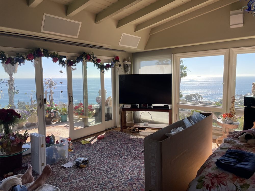 Living room with floor-to-ceiling windows overlooking the ocean, TV, couch, and holiday garland decor
