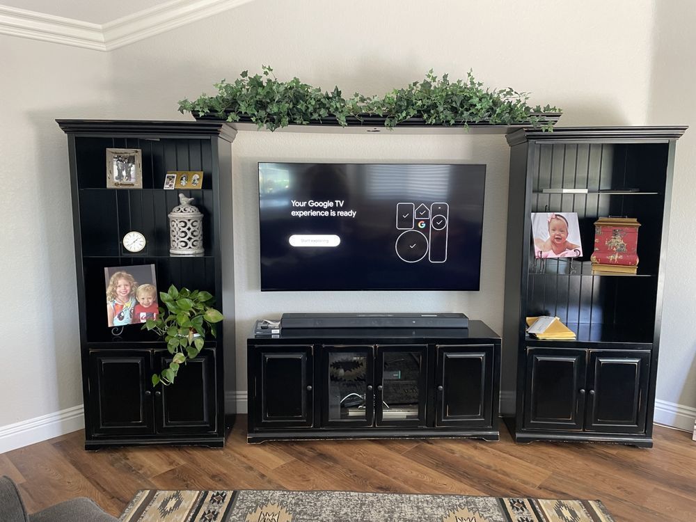 Living room entertainment center with a TV, black cabinets, and green plants on top