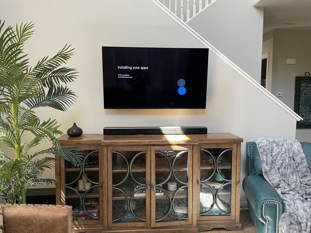 Living room with wall-mounted TV above a wooden cabinet, teal chair, and staircase in the background