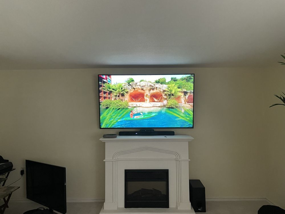 Living room with a wall-mounted TV above a white fireplace, showing a colorful tropical resort scene.