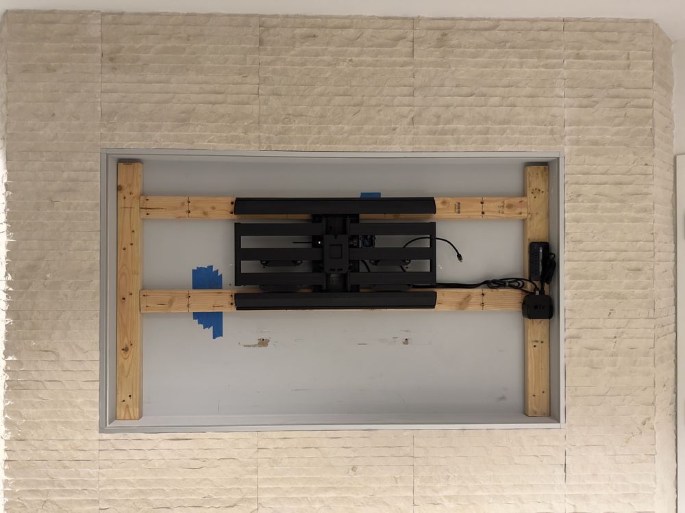 Wall-mounted monitor bracket in a framed opening, with wooden supports and blue tape.