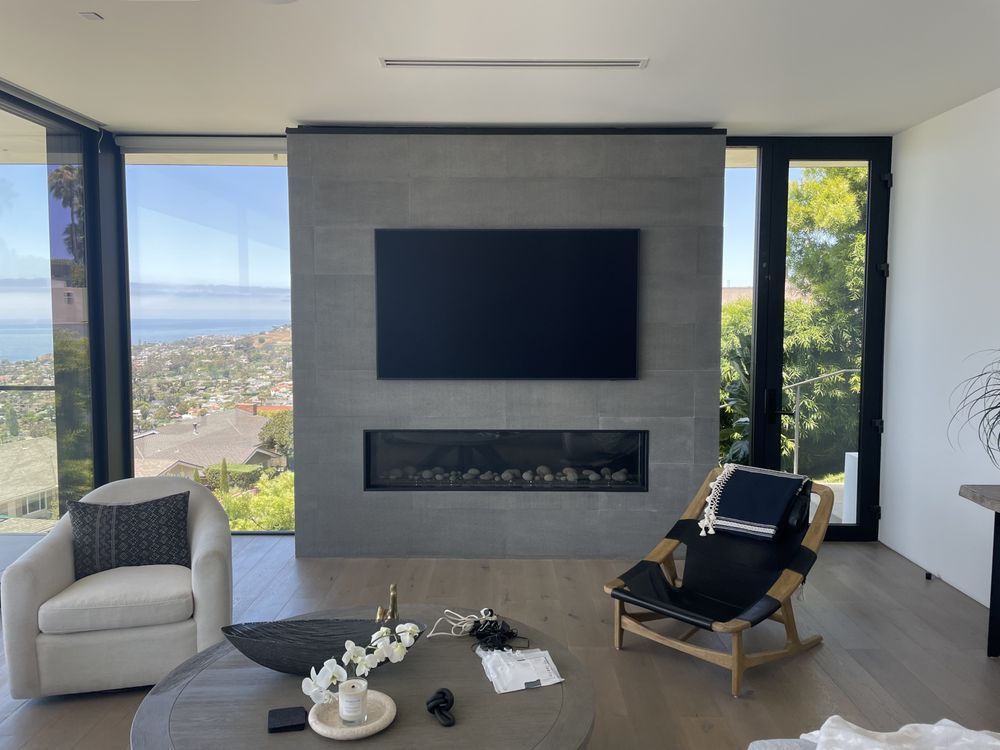 Modern living room with a large fireplace, panoramic windows, and city view; chairs and coffee table in front