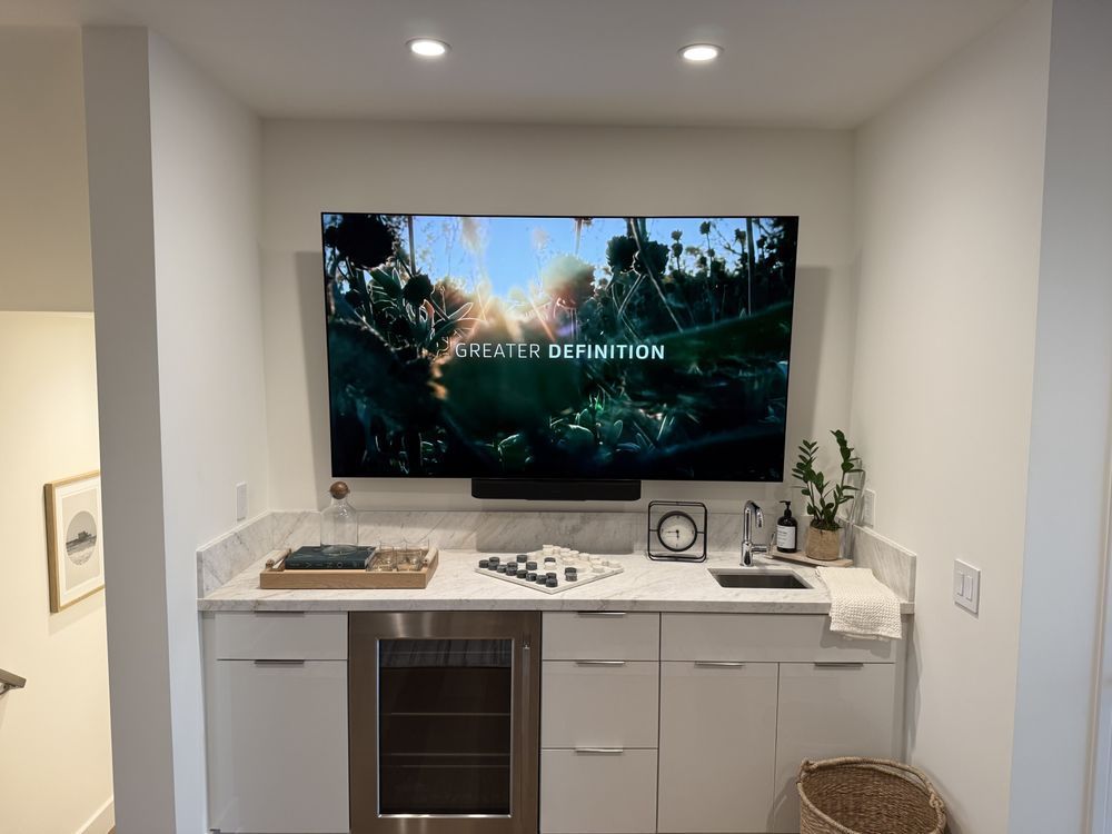 Compact wall-mounted TV above a white built-in cabinet in a small recessed living area with plants and decor