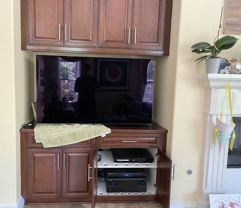 Wooden TV cabinet with built-in shelves, a dark television screen, and a towel draped over the counter