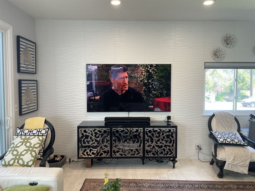 Modern living room with wall-mounted TV, decorative console, chairs, and bright windows