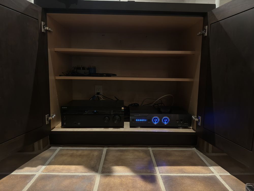 Open cabinet with shelves and electronics inside, including a black device and glowing blue audio controls.